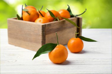 Taze, sulu mandalinalar ve bulanık yeşil arka planda beyaz ahşap masa üzerinde sandık.