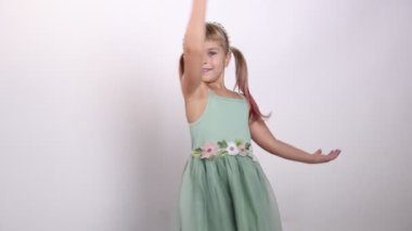 Saçbandı takmış gülümseyen küçük kız ve açık gri arka planda dans eden elbise.