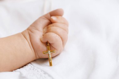 Vaftiz ayini. Yatakta altın haç tutan küçük bebek, yakın plan.