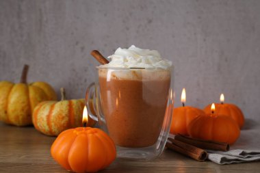 Cam bardakta kremalı balkabaklı latte, tarçın çubukları, taze sebzeler ve ahşap masada yanan mumlar, yakın plan.