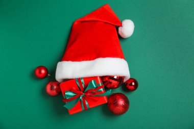 Noel Baba şapkası, Noel hediyesi ve yeşil arka planda takılar.