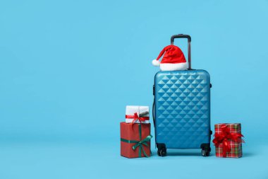 Noel tatili. Kırmızı bavul, Noel Baba şapkası ve açık mavi arka planda hediye kutuları. Metin için boşluk