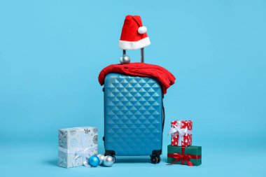 Noel tatili. Kırmızı bavul, Noel Baba şapkası, hediye kutuları ve açık mavi arka planda takılar.
