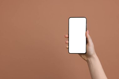 Kahverengi arka planda boş ekranlı akıllı telefonu olan bir kadın, yakın plan. Tasarım için model