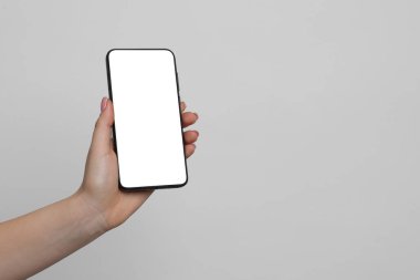 Açık gri arka planda boş ekranlı akıllı telefonu olan bir kadın, yakın plan. Tasarım için model