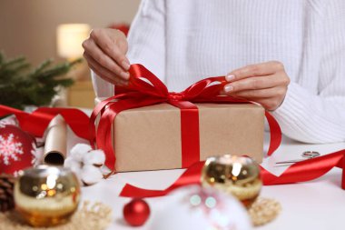 Beyaz masada Noel hediyesini paketleyen kadın, yakın plan.