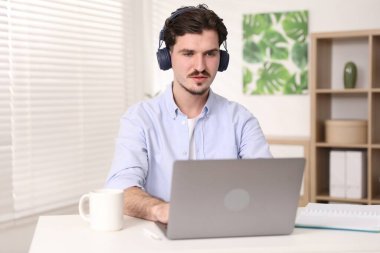 Kulaklıklı, laptoplu genç adam beyaz masada, kapalı bir masada.