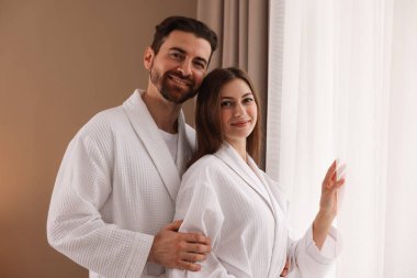 Otel odasının penceresinin yanında bornoz giyen mutlu çift.