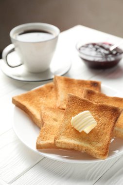 Beyaz ahşap masada tereyağı, reçel ve çay ile servis edilen taze kızarmış ekmek dilimleri.