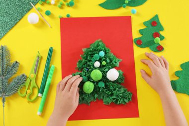 Küçük çocuk sarı masada Noel kartpostalı hazırlıyor. Çocuk el yapımı.