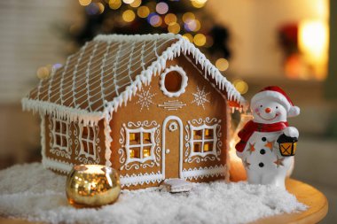 Güzel zencefilli kurabiye evi, kardan adam figürü, yanan mum ve kapalı alanda bulanık ışıklara karşı yapay kar, yakın plan. Noel atmosferi