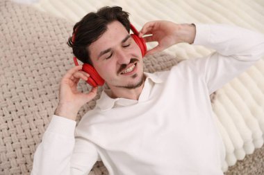 Kulaklıklı gülümseyen adam yatakta müzik dinliyor.