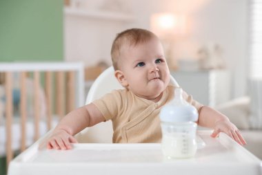 Evinde şezlongda yemek şişesi olan sevimli bir bebek.