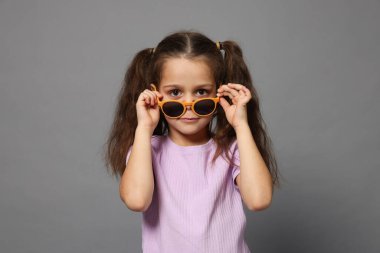 Gri arka planda güneş gözlüklü şirin bir kızın portresi.