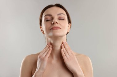 Açık gri arka planda boyun masajı yapan kadın.