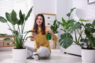 Bir kadın evdeki saksı bitkisine su püskürtüyor.