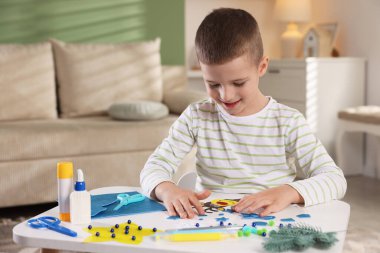 Küçük çocuk kapalı bir masada Noel kartı hazırlıyor. Çocuk el yapımı.