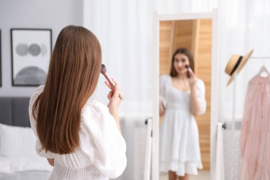 Güzel bir kadın aynanın yanında makyaj yapıyor.