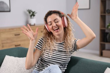 Kulaklıklı mutlu kadın evdeki kanepede müzik dinliyor.