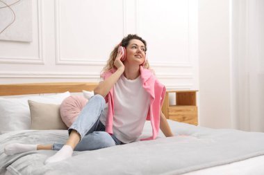 Kulaklıklı mutlu kadın evde beyaz duvarın yanında müzik dinliyor.