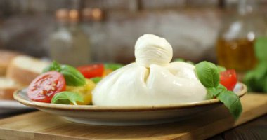 Ahşap masada nefis burrata peyniri, domates ve fesleğen yiyen kadın, yakın plan.