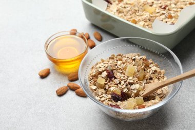 Tahıl yapıyorum. Yulaf gevreği, kurutulmuş meyve, badem fıstığı ve bal, gri desenli masa, yakın plan.