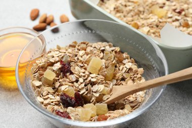 Tahıl yapıyorum. Yulaf gevreği, kurutulmuş meyve, badem fıstığı ve bal, gri desenli masa, yakın plan.