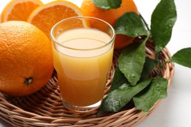 Taze portakal suyu, meyve ve yapraklar beyaz masada, yakın plan.