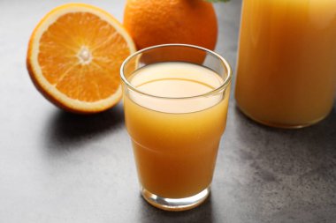 Taze portakal suyu ve meyveler gri masada, yakın plan.