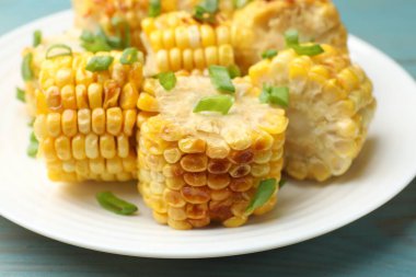 Mavi ahşap masada yeşil soğanlı ızgara mısır koçanı parçaları, yakın plan.