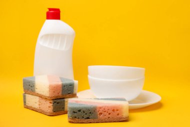Kitchen sponges, dish soap and dishware on yellow background. Space for text