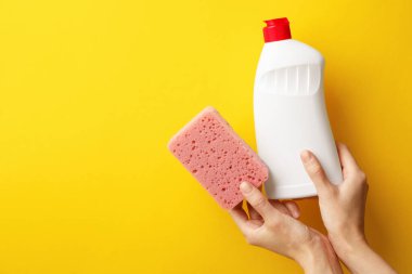 Turuncu arka planda sünger ve bulaşık deterjanı tutan kadın. Metin için boşluk