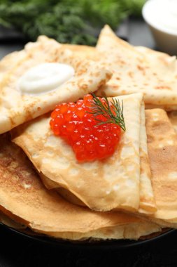 Kırmızı havyarlı leziz krepler ve siyah masada ekşi krema, yakın plan.
