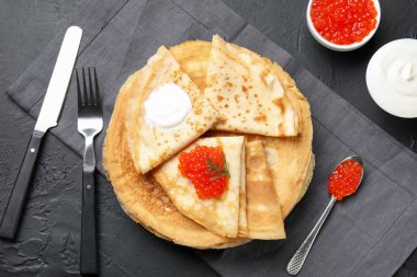 Kırmızı havyarlı ve ekşi kremalı leziz krepler siyah desenli masaya servis edilir, düz yatar.