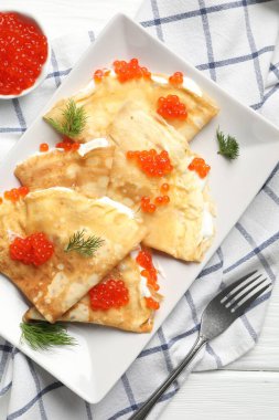 Beyaz ahşap masada servis edilen kırmızı havyarlı ve ekşi kremalı leziz krepler.