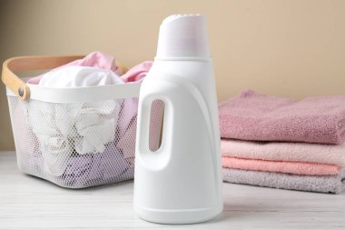 Çamaşır sepetini ve beyaz ahşap masanın üzerindeki deterjanı bej arka planda, yakın plan.