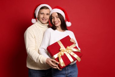 Kırmızı arka planda Noel Baba şapkalı mutlu çift