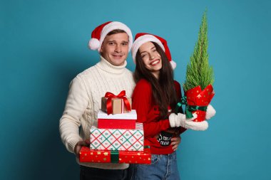 Noel Baba şapkalı mutlu bir çift ve açık mavi arka planda Noel hediyeleri.