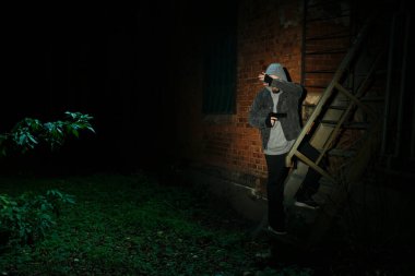 Kapüşonlu silahlı suçlu dışarıda tuğla binanın yanında, mesaj için yer var.