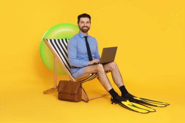 Dizüstü bilgisayarı ve yüzgeçleri olan bir iş adamı turuncu arka planda güverte koltuğunda baş parmak gösteriyor.