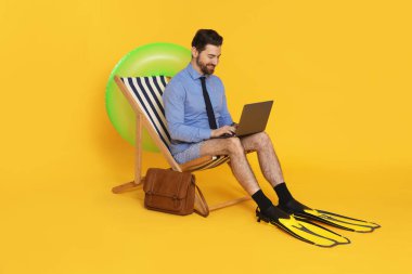 Dizüstü bilgisayarı ve yüzgeçleri olan bir iş adamı turuncu arka planda güverte koltuğunda baş parmak gösteriyor.