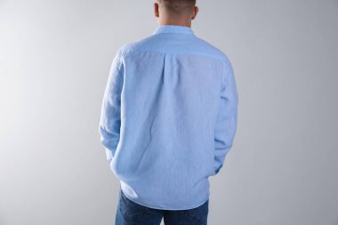 Gri duvarın yanında açık mavi gömlekli bir adam var.