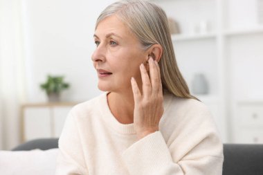 Evde işitme cihazı olan yaşlı bir kadın var.