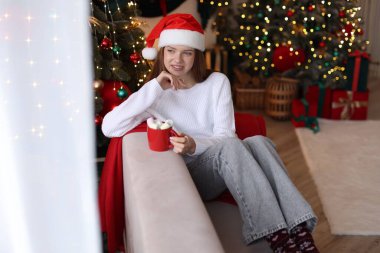 Evdeki bulanık ışıklara karşı elinde lokum dolu bir bardak sıcak içecek tutan güzel bir genç kız. Noel atmosferi