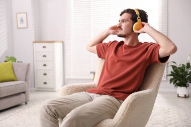 Kulaklıklı genç adam evdeki koltukta müzik dinliyor.