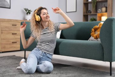 Kulaklıklı mutlu kadın evdeki kanepenin yanında dans ediyor.