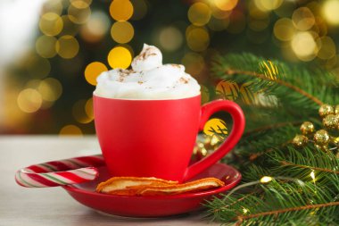 Krem şantili Aromatik kahve, kurutulmuş portakal dilimleri ve beyaz ahşap masada Noel dekoru bulanık ışıklara karşı, yakın çekim