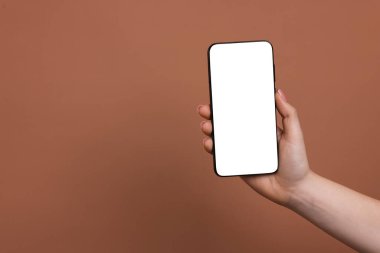 Kahverengi arka planda boş ekranlı akıllı telefonu olan bir kadın, yakın plan. Tasarım için model