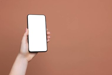 Kahverengi arka planda boş ekranlı akıllı telefonu olan bir kadın, yakın plan. Tasarım için model