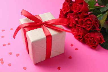 Sevgililer Günün kutlu olsun. Hediye kutusu, konfeti ve pembe arka planda kırmızı güller, yakın plan.